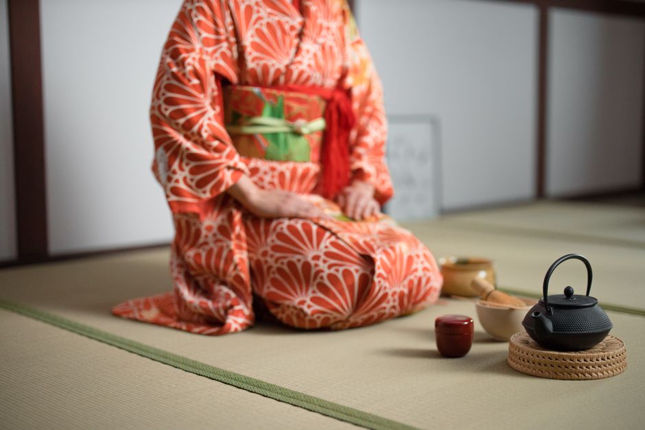Woman in kimono performing a traditional Japanese tea ceremony, indoors.
