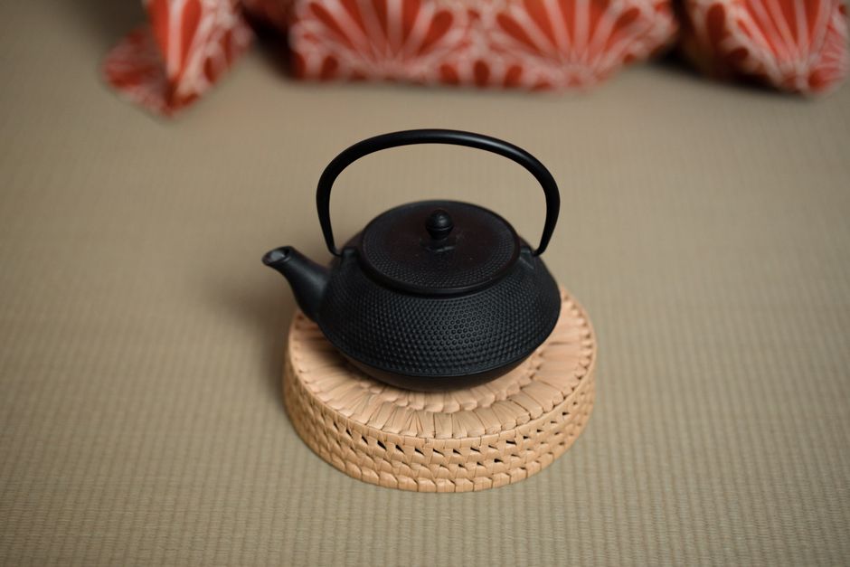 A black cast iron teapot sits elegantly on a bamboo coaster, ideal for tea ceremonies.