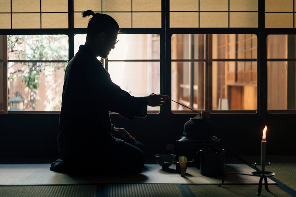 Silhouette of a person performing a traditional Japanese tea ceremony indoors near a window.